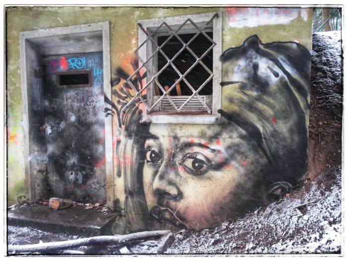Graffiti eines Gesichtsporträts an der Wand eines verfallenen Betongebäudes mit Tür und vergittertem Fenster im Schnee