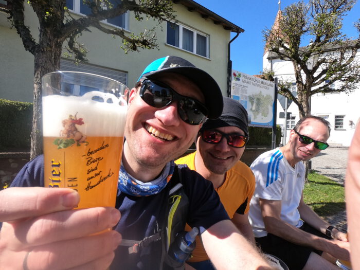 Drei lächelnde Männer, Thorsten, Flo und Hansi, mit Sonnenbrillen machen draußen ein Selfie und einer hält ein Glas Bier in die Kamera