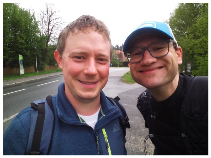 Zwei lächelnde Männer, Thomas und Thorsten, machen ein Selfie im Freien neben einer Straße