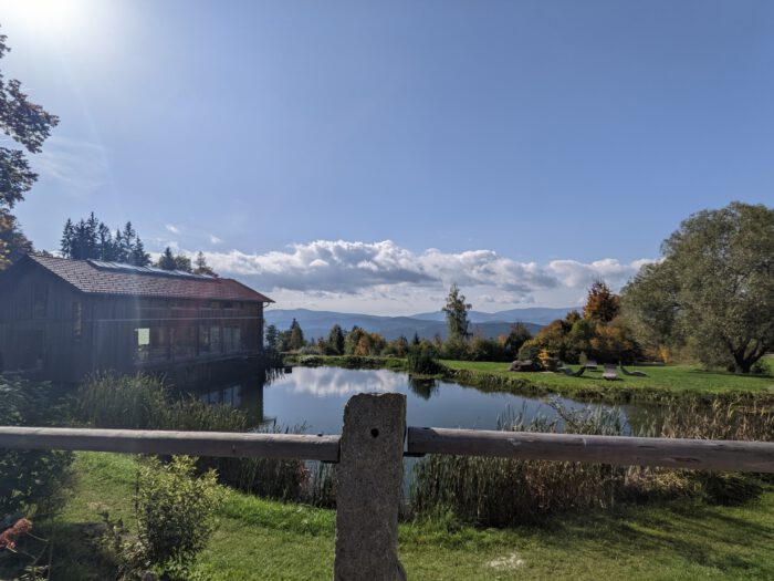 Holzgebäude an einem Teich mit Bergpanorama im Hintergrund unter blauem Himmel