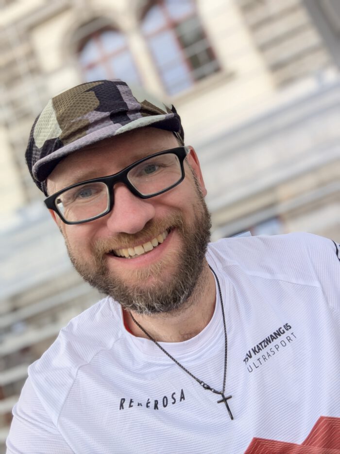 Thorsten Hoyer lächelnd in Sportkleidung mit Brille und Camouflage-Mütze