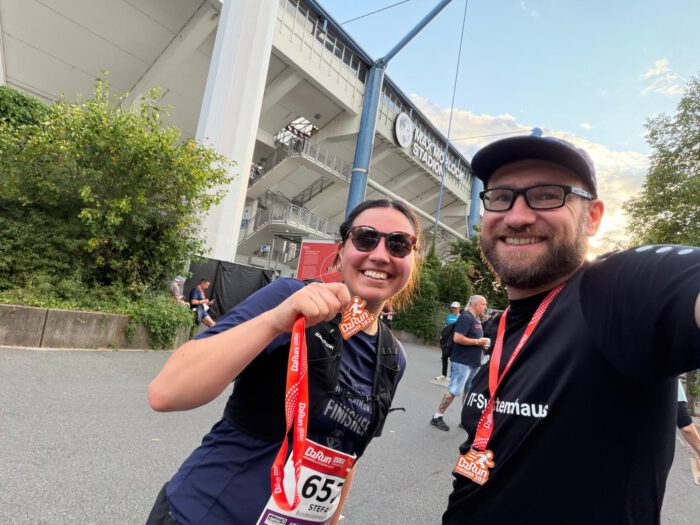 Thorsten und Steffi lächeln mit ihren B2Run-Finisher-Medaillen vor dem Max-Morlock-Stadion