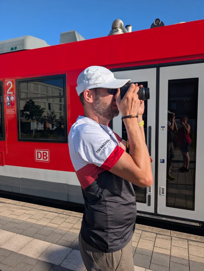 Ein Wanderer fotografiert am Bahnsteig vor einem roten Zug der Gräfenbergbahn