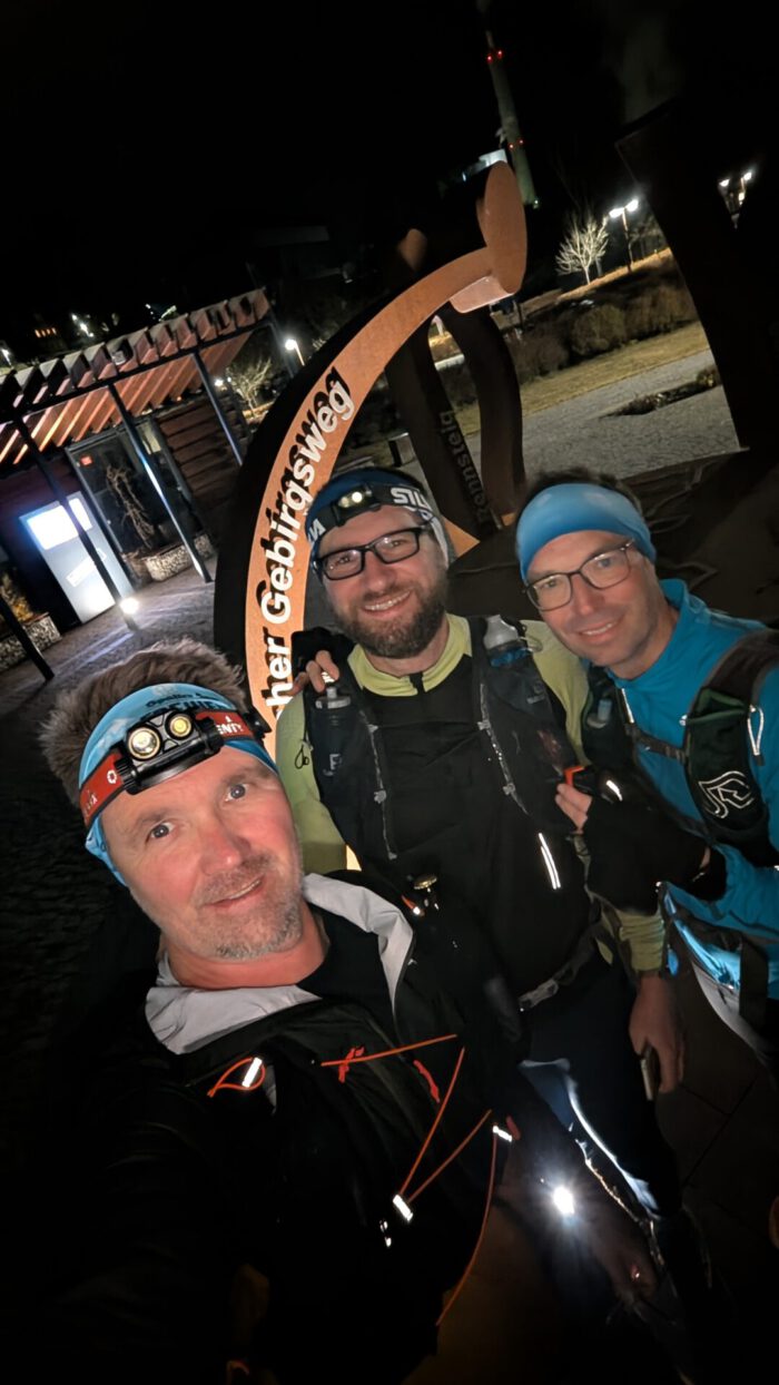 Peter, Flo und der Autor lächeln nachts mit Stirnlampen und Wanderrucksäcken am Zielpunkt des Fränkischen Gebirgswegs