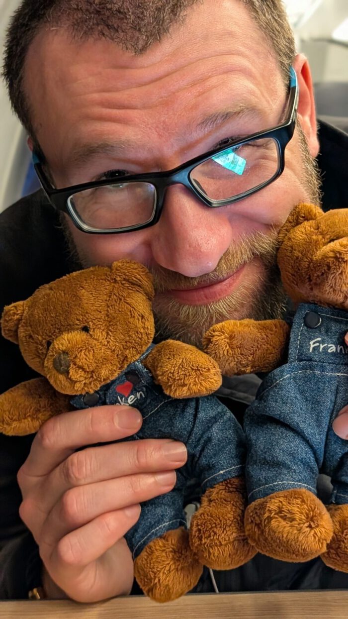 Ein lächelnder Mann mit Brille hält zwei kleine Teddybären in Latzhosen mit der Aufschrift Franken