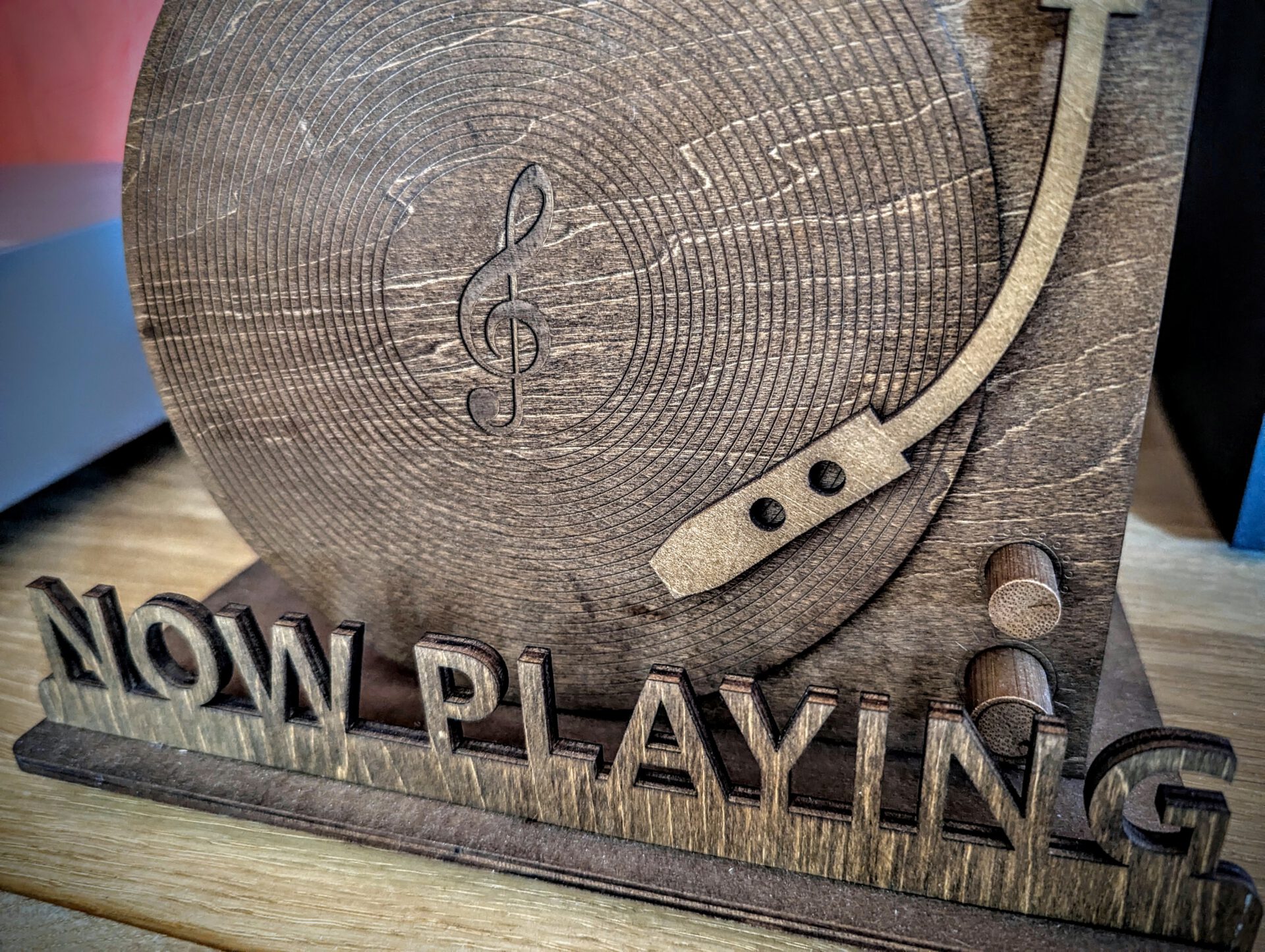 Holzaufsteller mit der Aufschrift NOW PLAYING und einem stilisierten Plattenspieler-Design mit Notenschlüssel