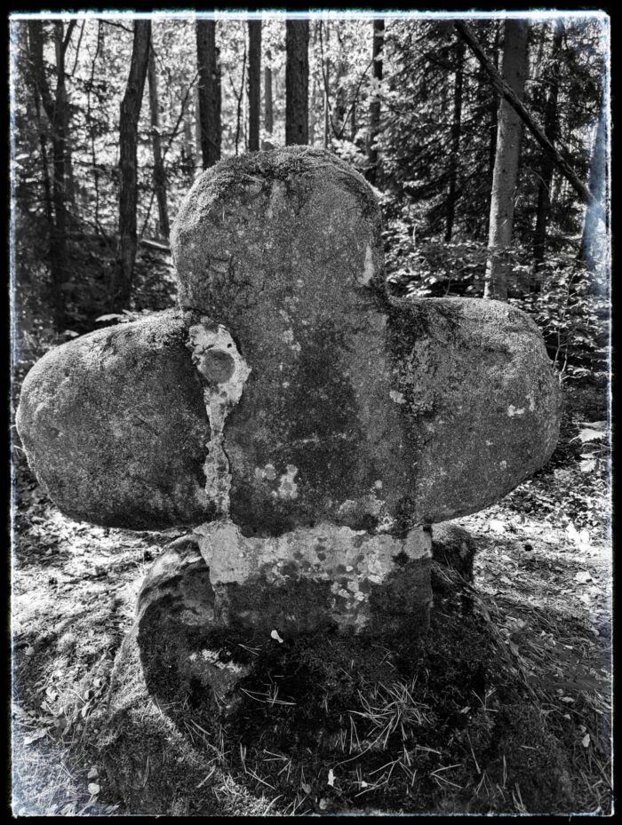 Verwitterter und bemooster historischer Kreuzstein aus Stein mitten im Wald