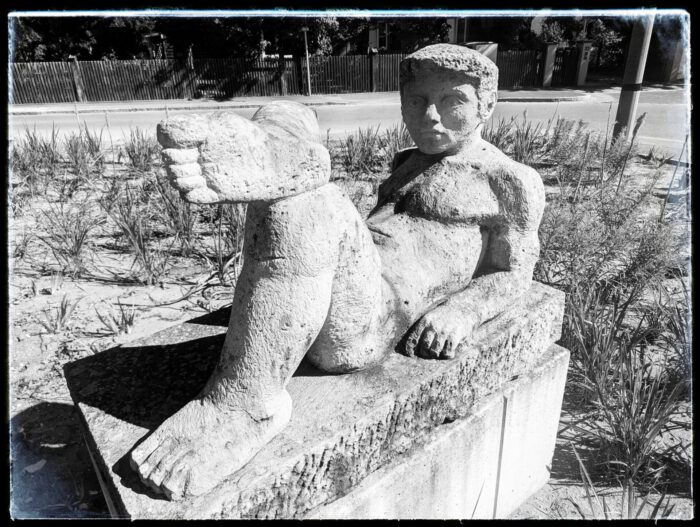 Steinskulptur eines liegenden Mannes mit angewinkeltem Bein auf einem Sockel