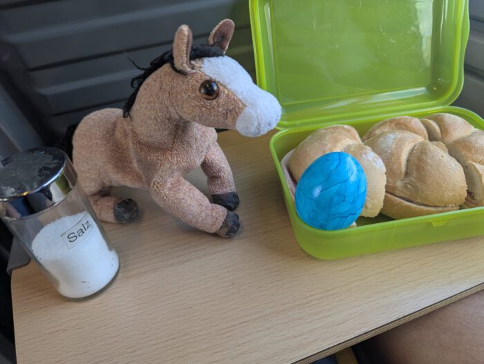 Pferdinand, ein Salzstreuer und eine grüne Brotbox mit Brötchen und einem blauen Ei auf einem Tisch