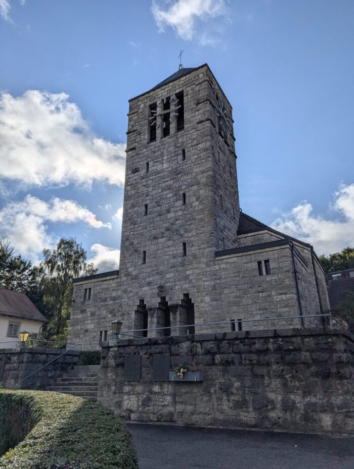 Kirche aus Naturstein mit einem hohen quadratischen Glockenturm unter bewölktem Himmel