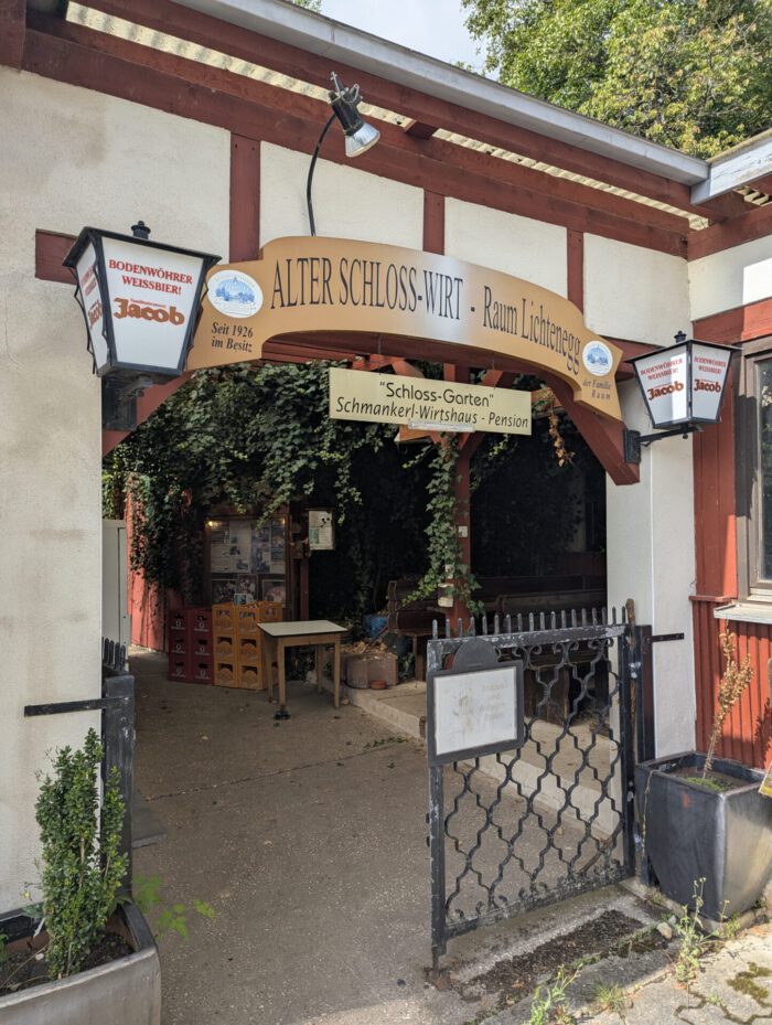 Eingang zum Schmankerl-Wirtshaus Alter Schloss-Wirt mit beschriftetem Bogen und Eisengittertor