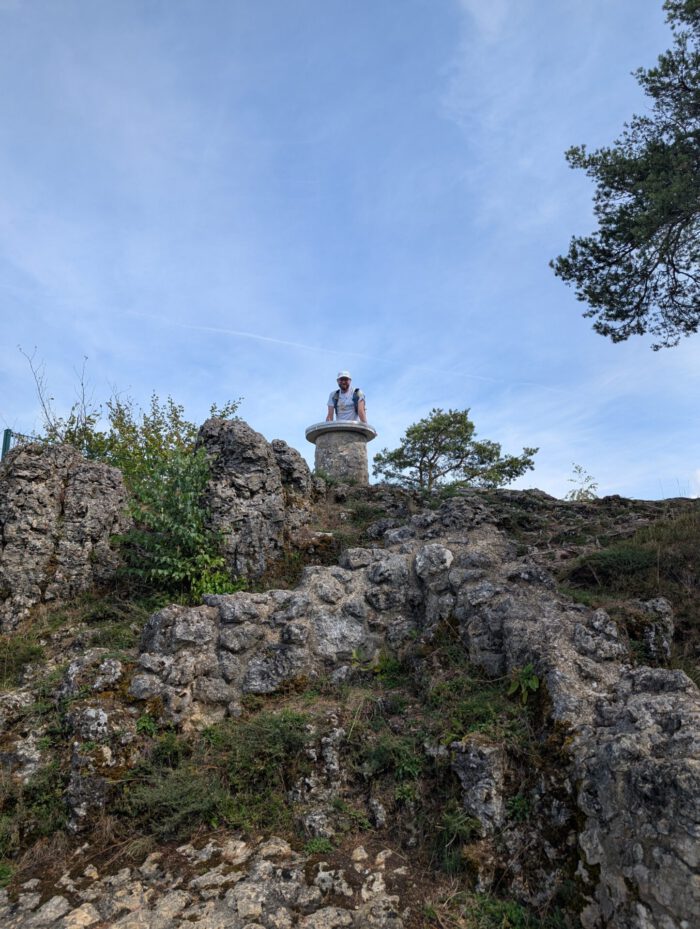 Thorsten auf einem felsigen Aussichtspunkt hinter einer runden Orientierungstafel aus Stein auf der Burg Lichtenegg