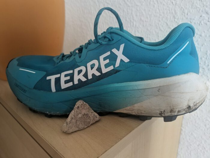 Türkisblauer Adidas Terrex Agravic 3 Trailschuh mit weißem Schriftzug neben einem kleinen Stein