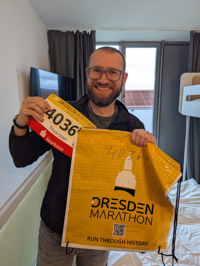 Lächelnder Thorsten zeigt seine Startnummer 4036 mit dem Namen Thorsten und seinen Beutel für den Dresden-Marathon