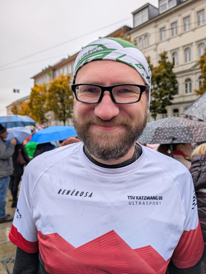 Lächelnder Thorsten mit Brille, Vollbart und Laufshirt des TSV Katzwang 05 Ultrasport draußen im Regen