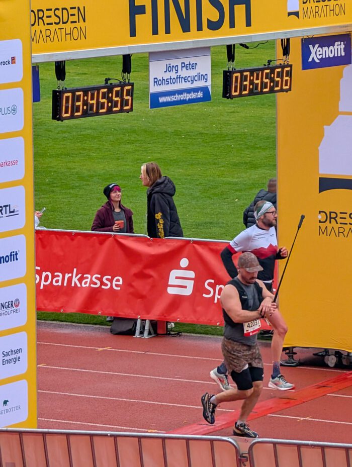 Läufer überqueren die Ziellinie beim Dresden-Marathon unter einer digitalen Zeitanzeige von 03:45:55
